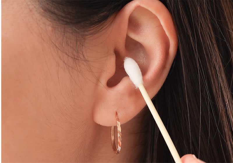 Ohrreinigung mit Wattestäbchen und Ohrring am Ohr