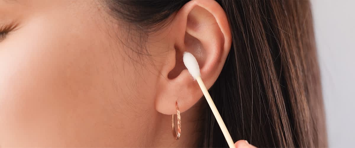 Ohrreinigung mit Wattestäbchen und Ohrring am Ohr
