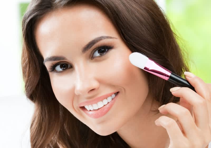 Dunkelhaarige Frau die sich mit Pinsel über eine Wange streicht