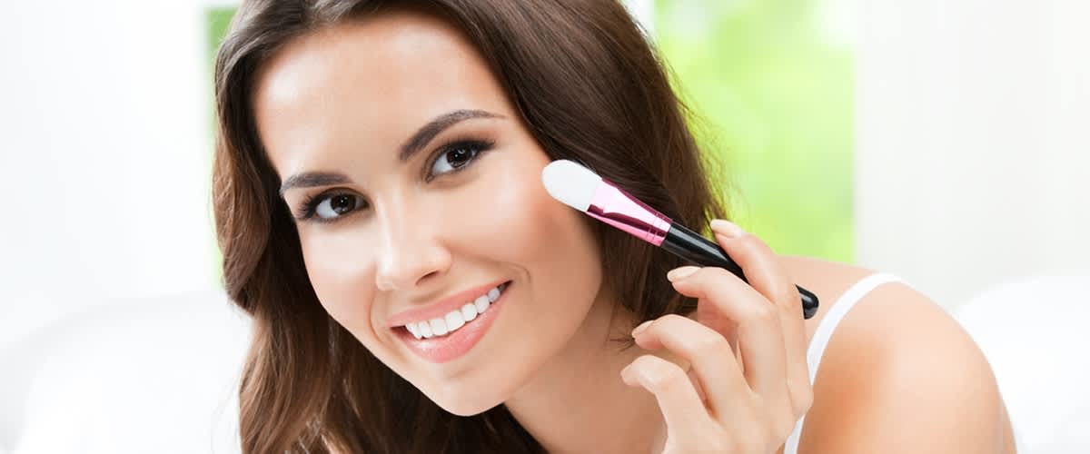 Dunkelhaarige Frau die sich mit Pinsel über eine Wange streicht