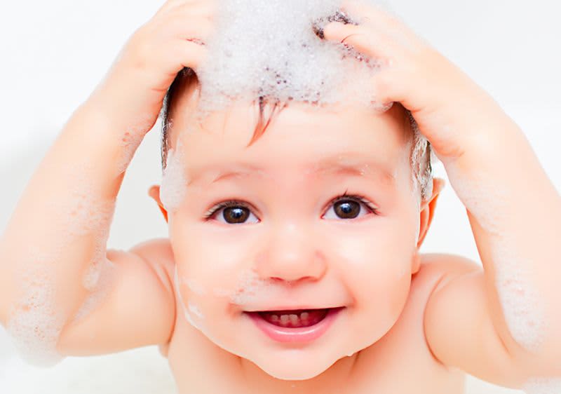 Baby in Badewanne mit beiden Händen am Kopf und Schaum auf den Haaren