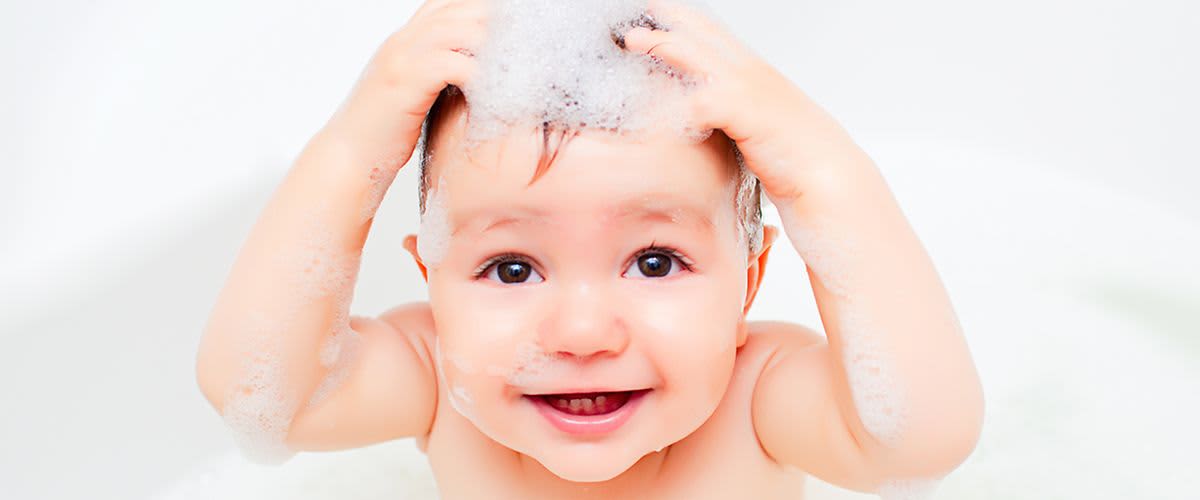 Baby in Badewanne mit beiden Händen am Kopf und Schaum auf den Haaren