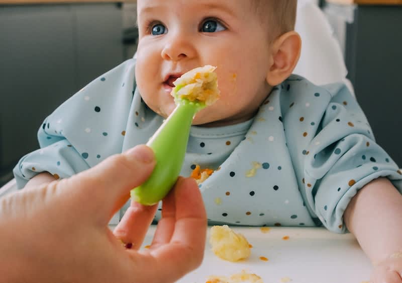 Baby in Hochstuhl wird mit einem Löffel brei gefüttert