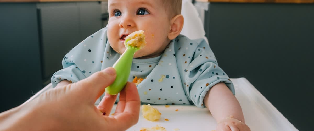 Baby in Hochstuhl wird mit einem Löffel brei gefüttert