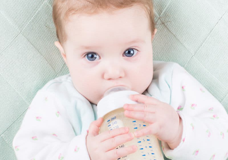Baby mit blauen Augen und Babyfläschen im Mund