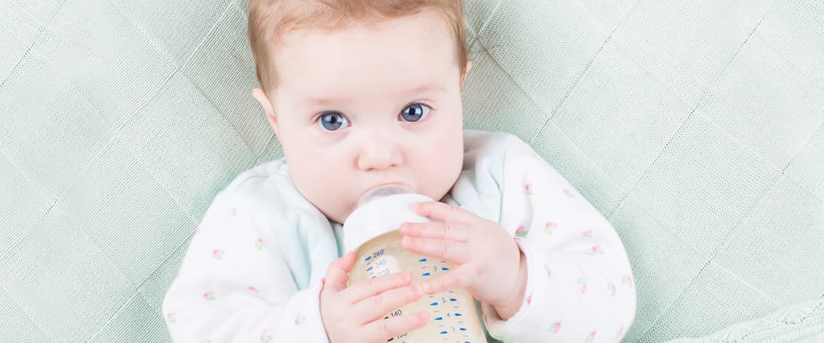 Baby mit blauen Augen und Babyfläschen im Mund