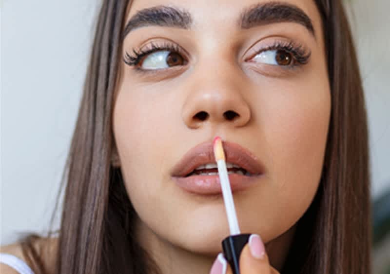 Frau trägt sich Lipgloss auf