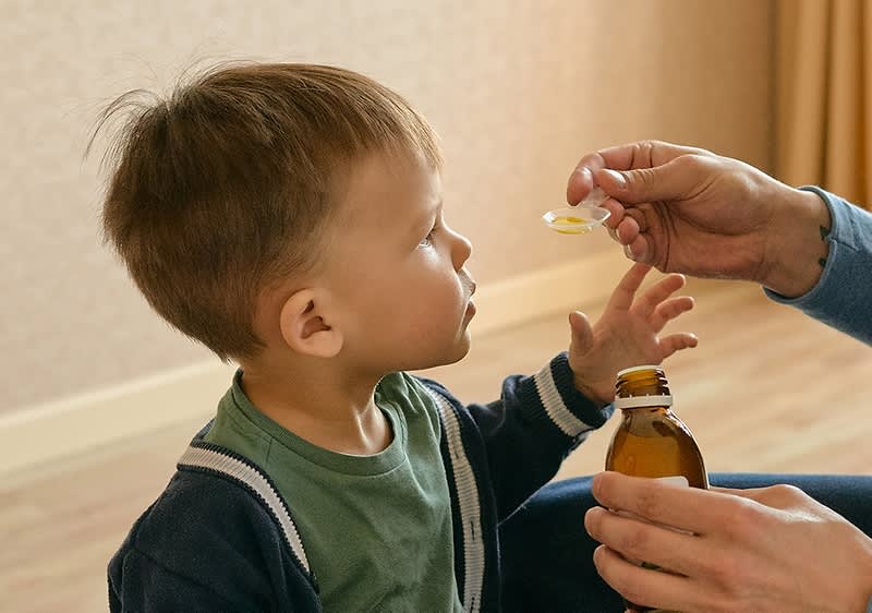 Mama gibt Sohn Medikament auf Loeffel