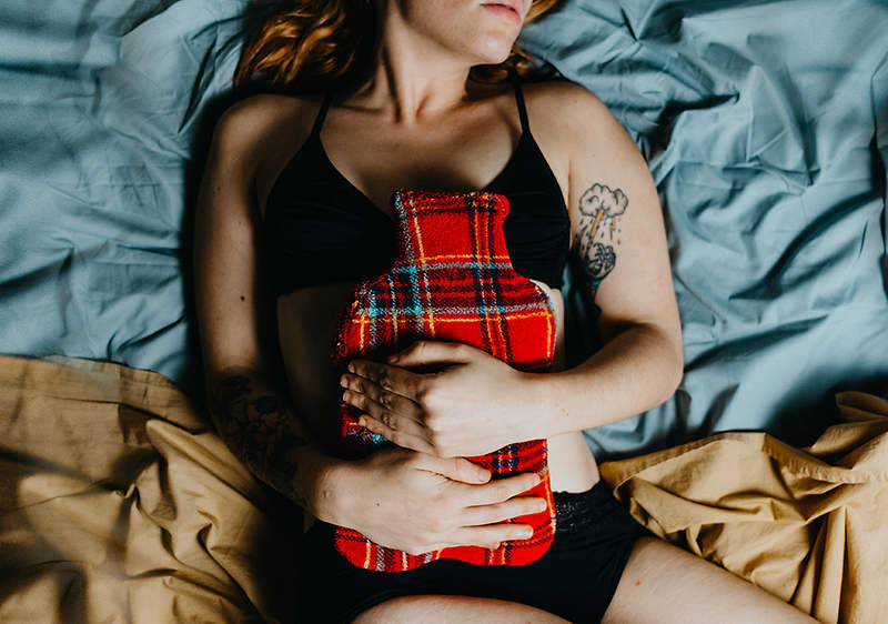 Frau liegt mit Wärmflasche im Bett