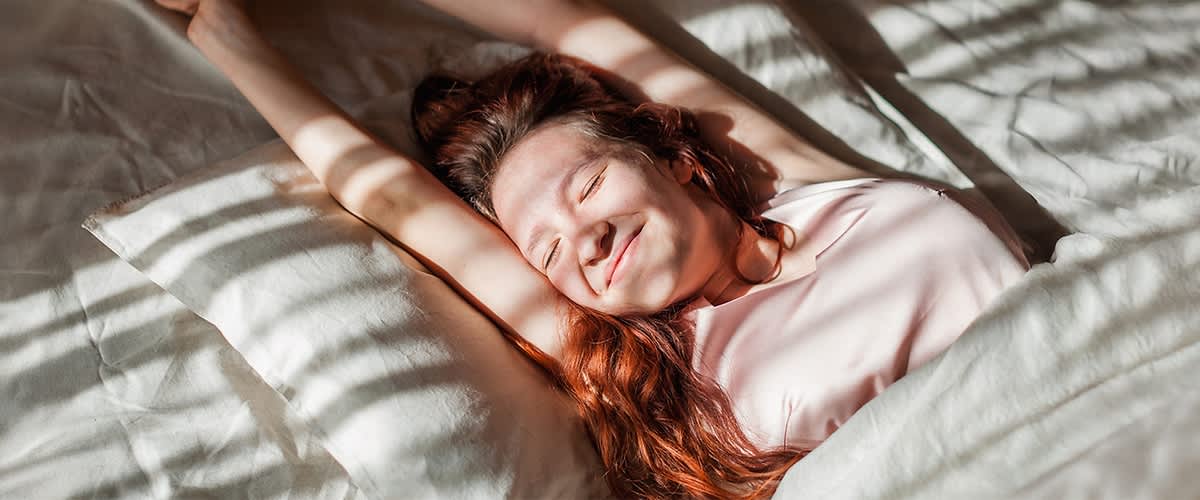 Frau mit langen roten Haaren liegt entspannt im Bett