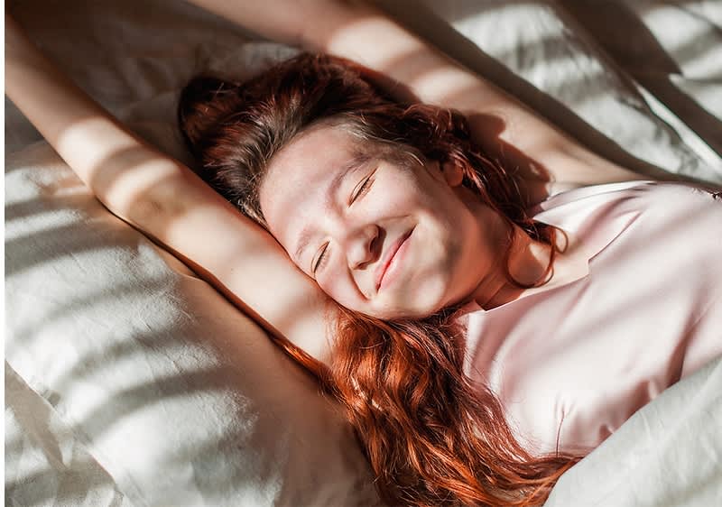 Frau mit langen roten Haaren liegt entspannt im Bett
