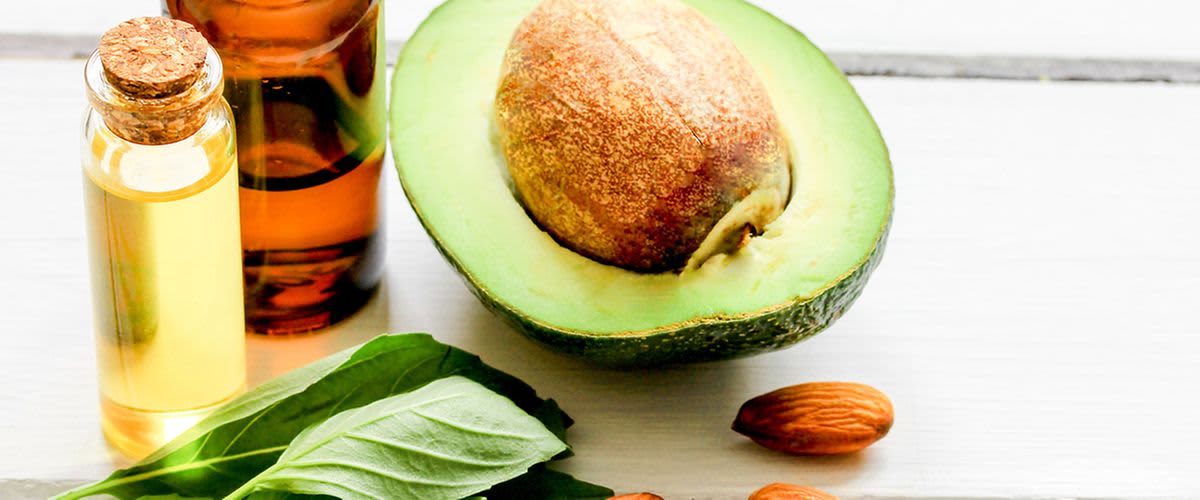 Halbe Avocado neben Mandeln und Fläschchen mit Öl