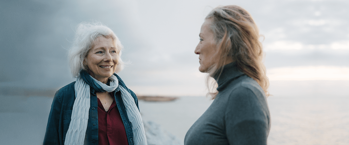 Zwei ältere Damen lächeln sich an