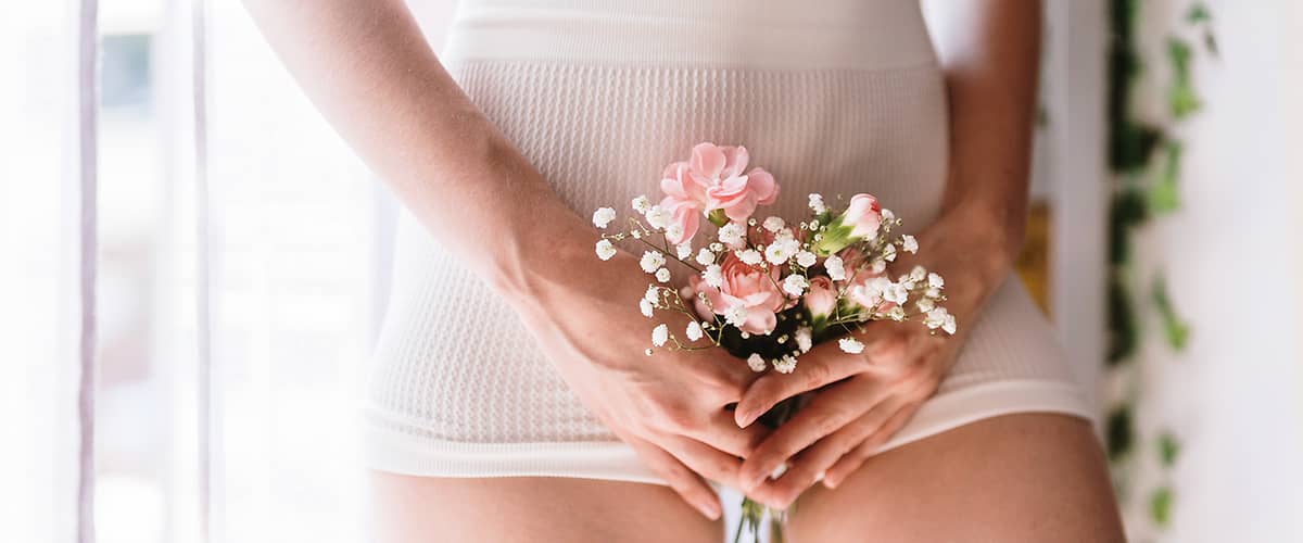 Frau hält Blumen vor ihrem Intimbereich