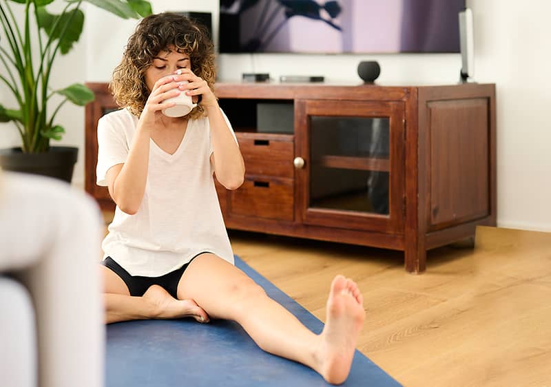 Frau trinkt Kaffee auf ihrer Yoga-Matte
