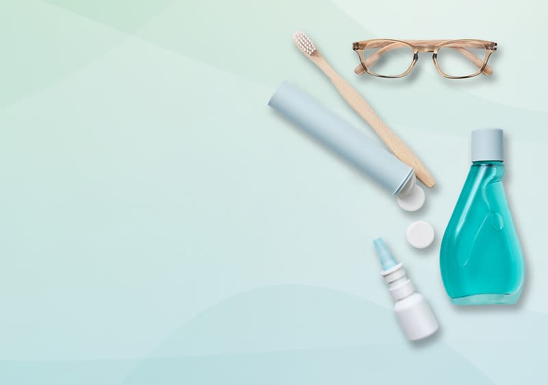 Eine Zahnbürste, eine Brille, eine blaue Mundwasserflasche, ein Nasenspray und eine Zahnpastatube auf einem hellgrünen Hintergrund