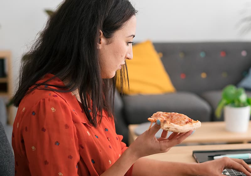 Frau isst vor ihrem Laptop