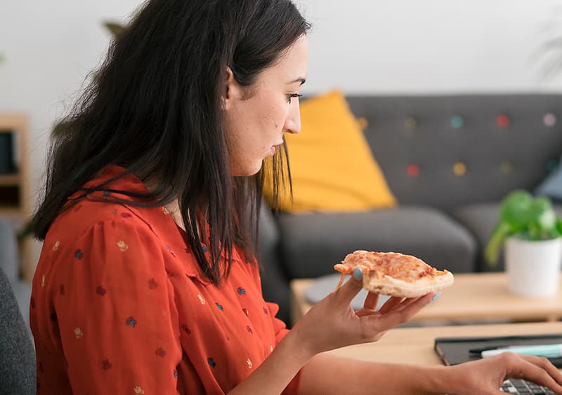 Frau isst vor ihrem Laptop