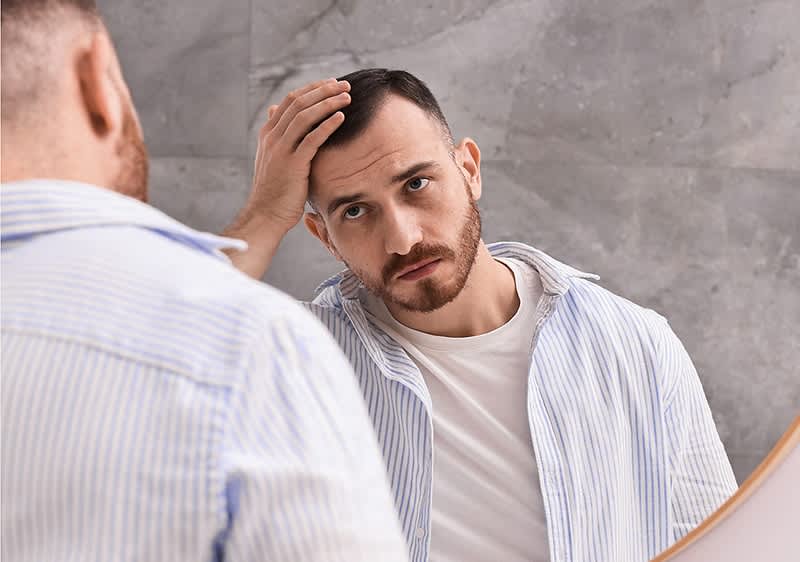 Mann im gestreiften Hemd betrachtet sich im Spiegel