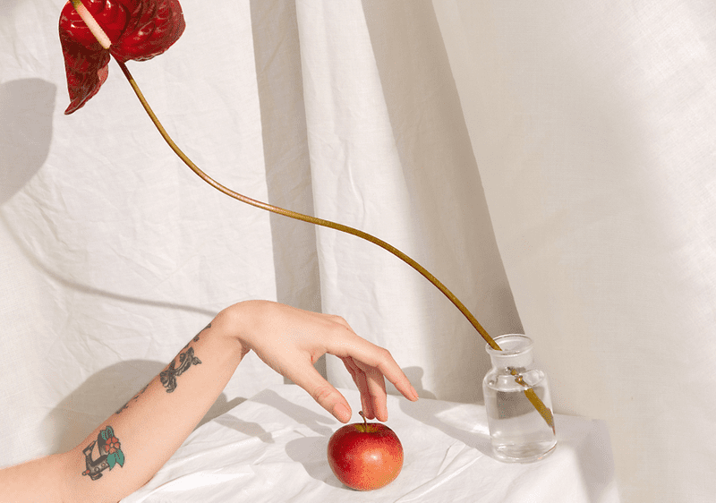 Blume in Vase mit Hand und Apfel auf weißem Hintergrund