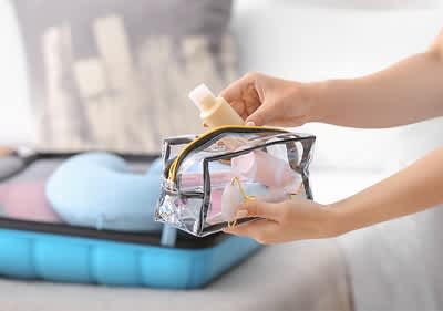 Reiseutensilien in transparenter Tasche vor gepacktem Koffer