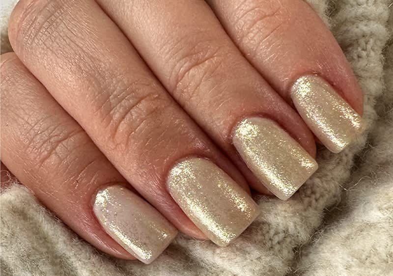 Glitzernde Fingernägel mit hellem Nagellack auf Wollstoff