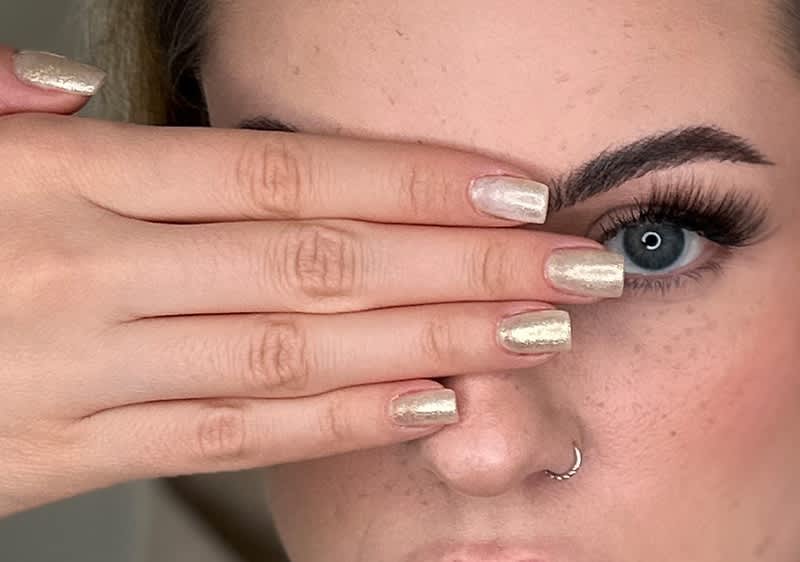 Hand mit hell lackierten Fingernägeln vor verschwommenem Gesicht