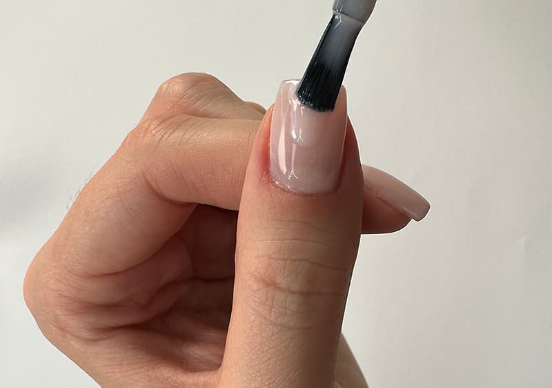 Hand, die den Daumen mit einem Pinsel hellrosé lackiert, sichtbarer feuchter Nagellack auf dem Nagel