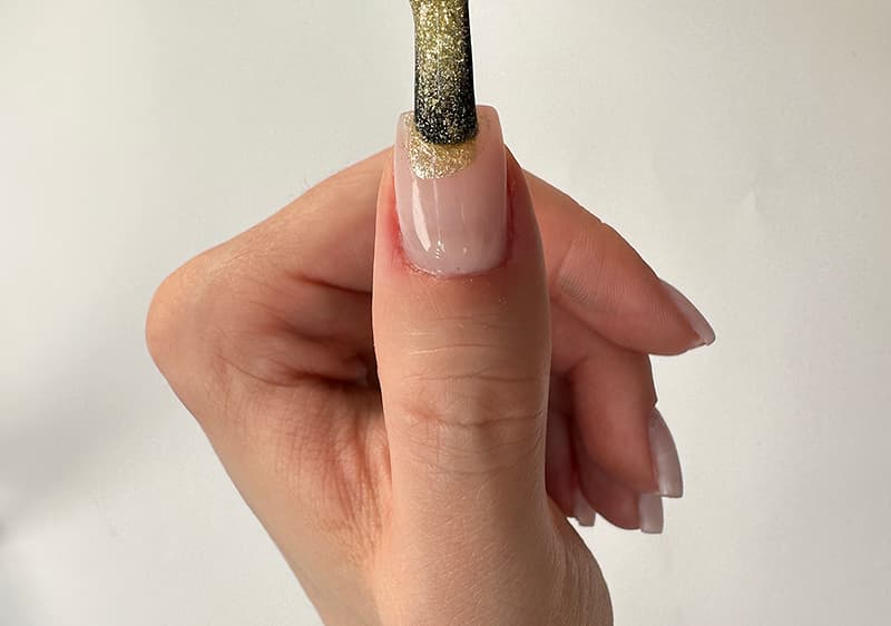 Hand mit Daumen nach oben, auf dem Daumennagel wird mit einem Pinsel goldener Glitzerlack aufgetragen