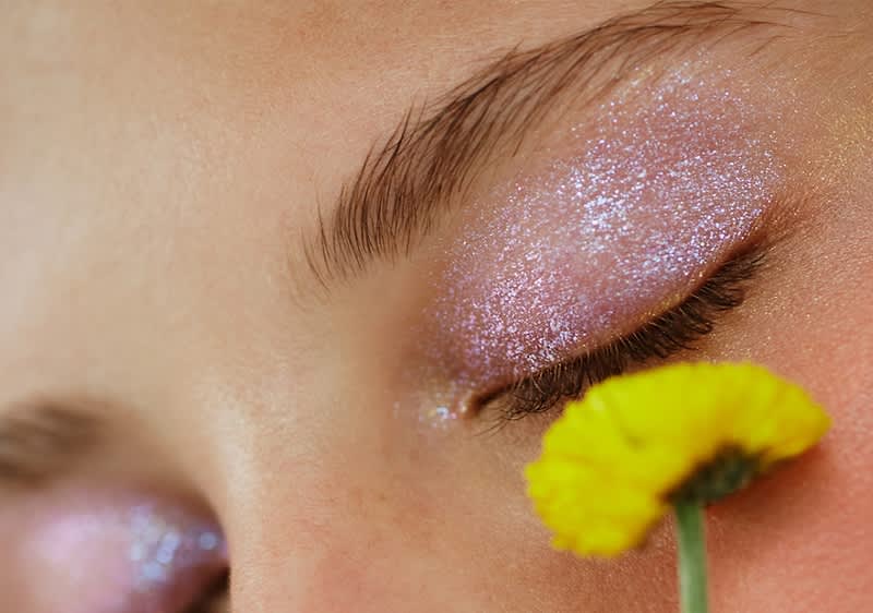 Glitzerndes Augen-Make-up mit geschlossenen Augen und gelber Blume