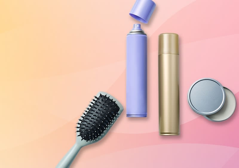 Eine lila Sprühflasche, eine goldene Flasche und eine schwarze Haarbürste auf einem rosa-gelben Hintergrund