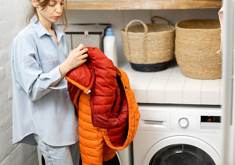 Frau mit Daunenjacke vor Waschmaschine