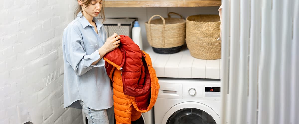 Frau mit Daunenjacke vor Waschmaschine