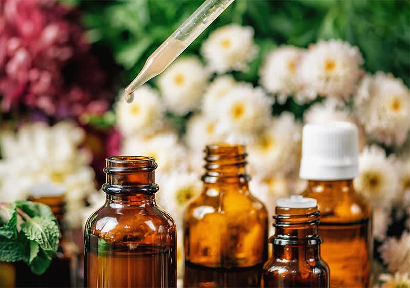 Ätherische Öle mit Pipette und Blumen im Hintergrund