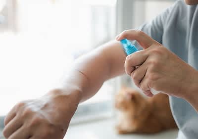 Desinfektionsspray auf Arm mit Katze im Hintergrund
