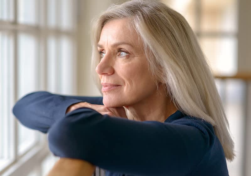 Frau mit langen blonden Haaren lehnt an Fensterbank