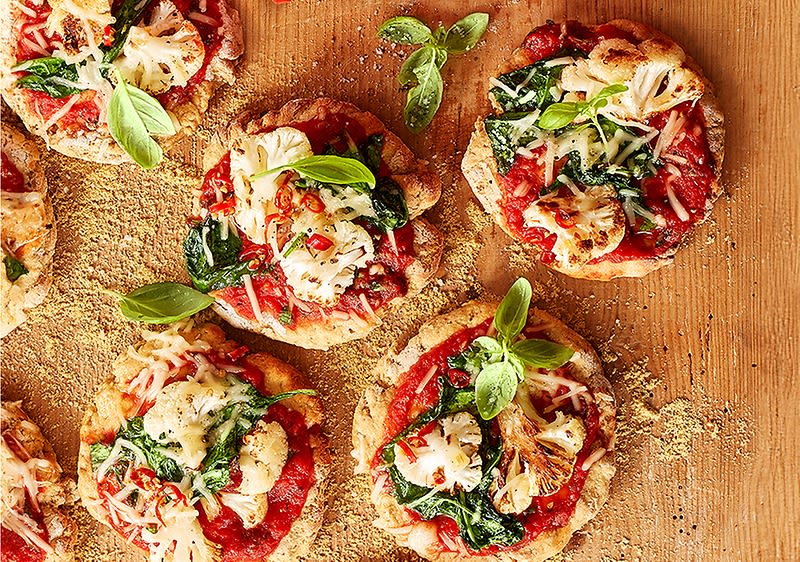 Fünf kleine Pizzen mit Tomatensauce, geschmolzenem Käse, Spinat und Basilikumblättern auf einem Holzbrett