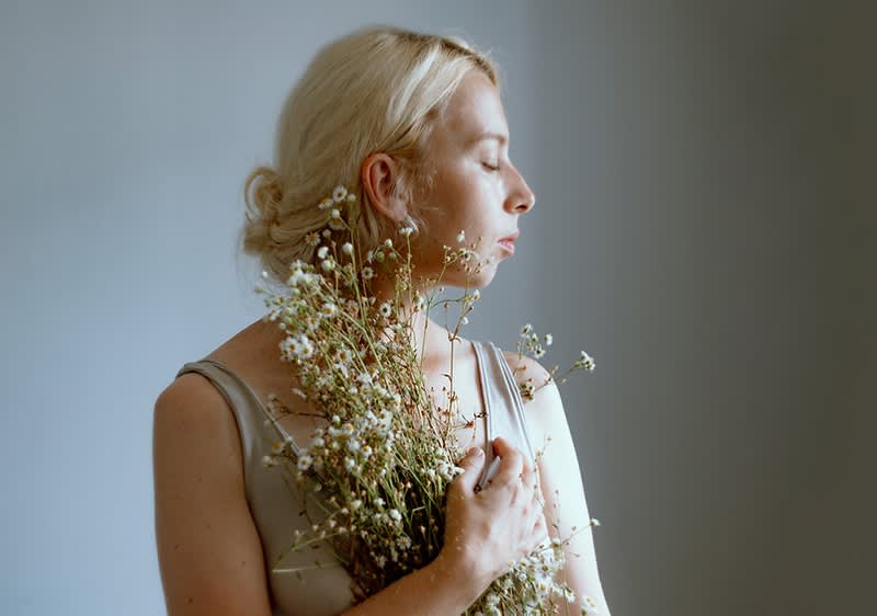 Blonde Frau mit Blumenstrauß in beigem Top vor grauem Hintergrund