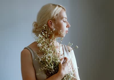 Blonde Frau mit Blumenstrauß in beigem Top vor grauem Hintergrund