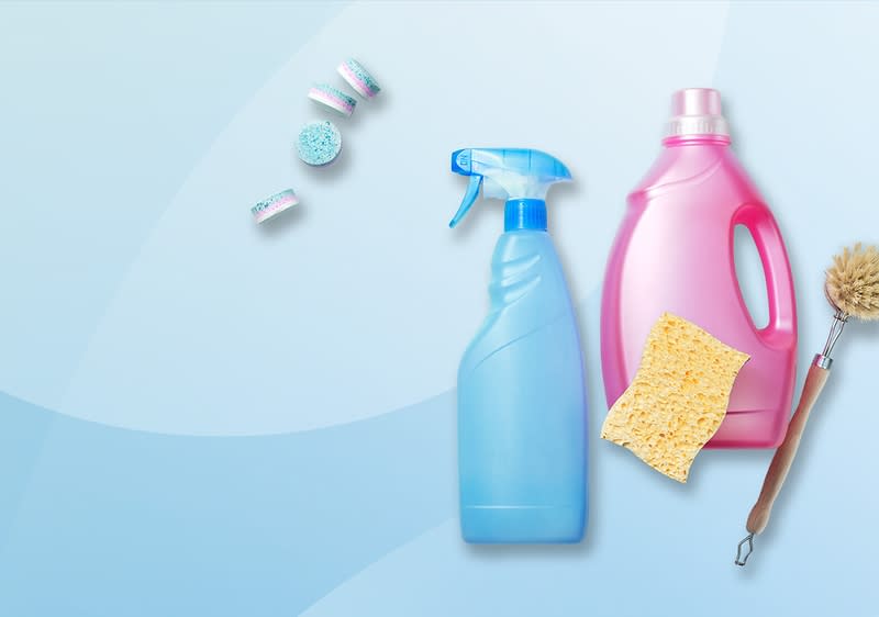 Eine blaue Sprühflasche, eine pinke Waschmittelflasche, ein gelber Schwamm, eine Bürste und drei Spülmaschinentabs auf blauem Hintergrund