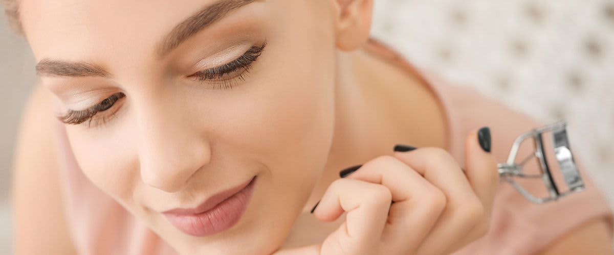 Frau mit schönen Wimpern und Wimpernzange in der Hand
