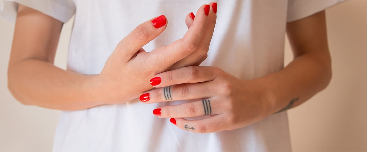 Rote Fingernägel und Tattoos auf Händen vor weißem Shirt