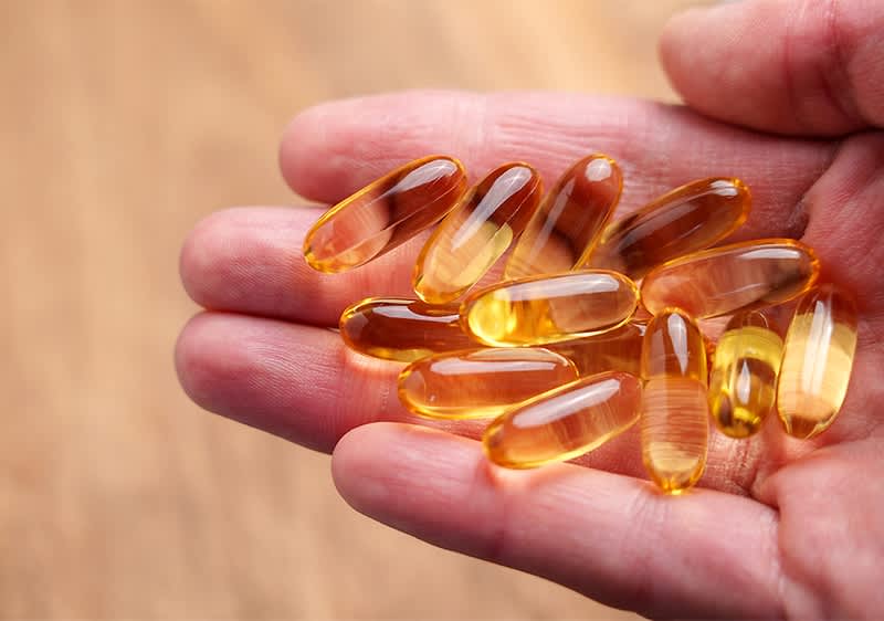 Omega-3-Kapseln in einer Hand auf Holzhintergrund