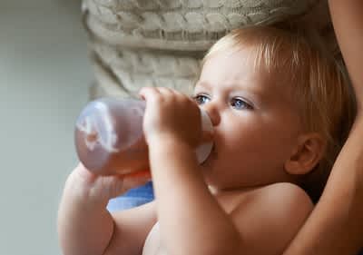 Baby trinkt aus Flasche in Armen einer Person