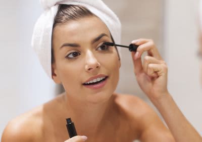 Frau mit Haarturban trägt sich Mascara vor Spiegel auf