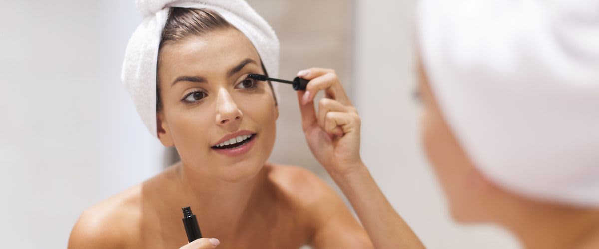 Frau mit Haarturban trägt sich Mascara vor Spiegel auf