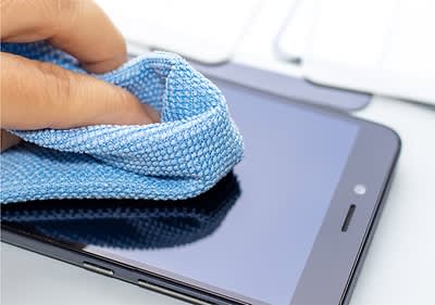 Eine Hand reinigt mit einem blauen Mikrofasertuch die Oberfläche eines Smartphones