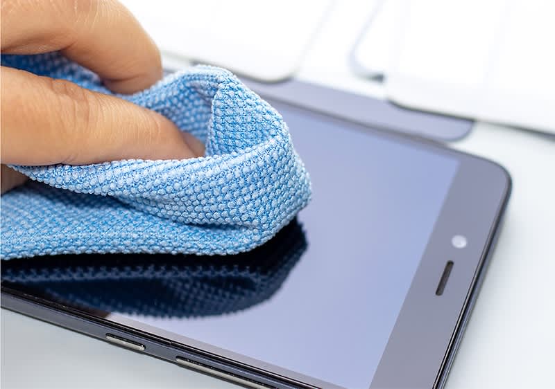 Eine Hand reinigt mit einem blauen Mikrofasertuch die Oberfläche eines Smartphones