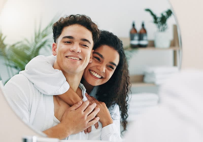 Paar umarmt sich vor einem Spiegel mit Pflanzen im Hintergrund