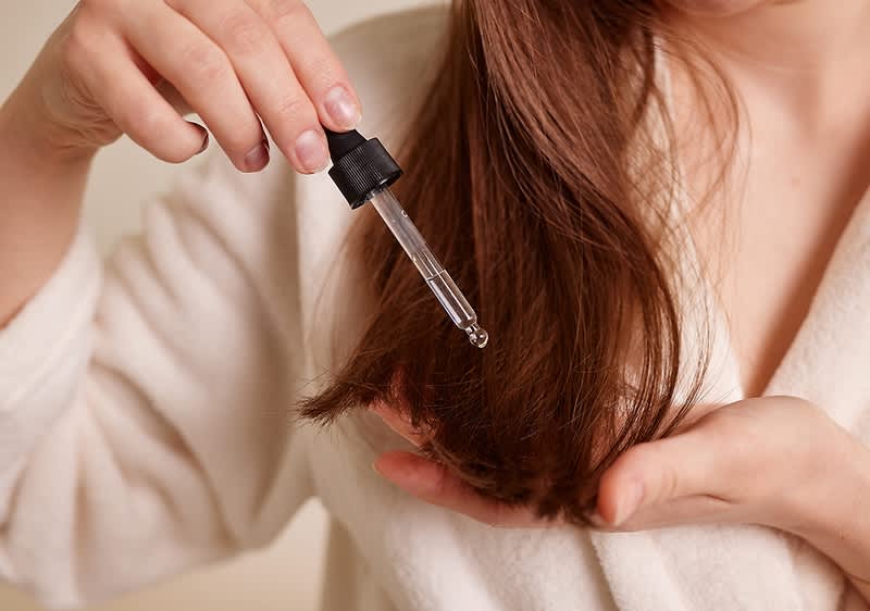 Frau tropft Arganöl auf die Haarspitzen